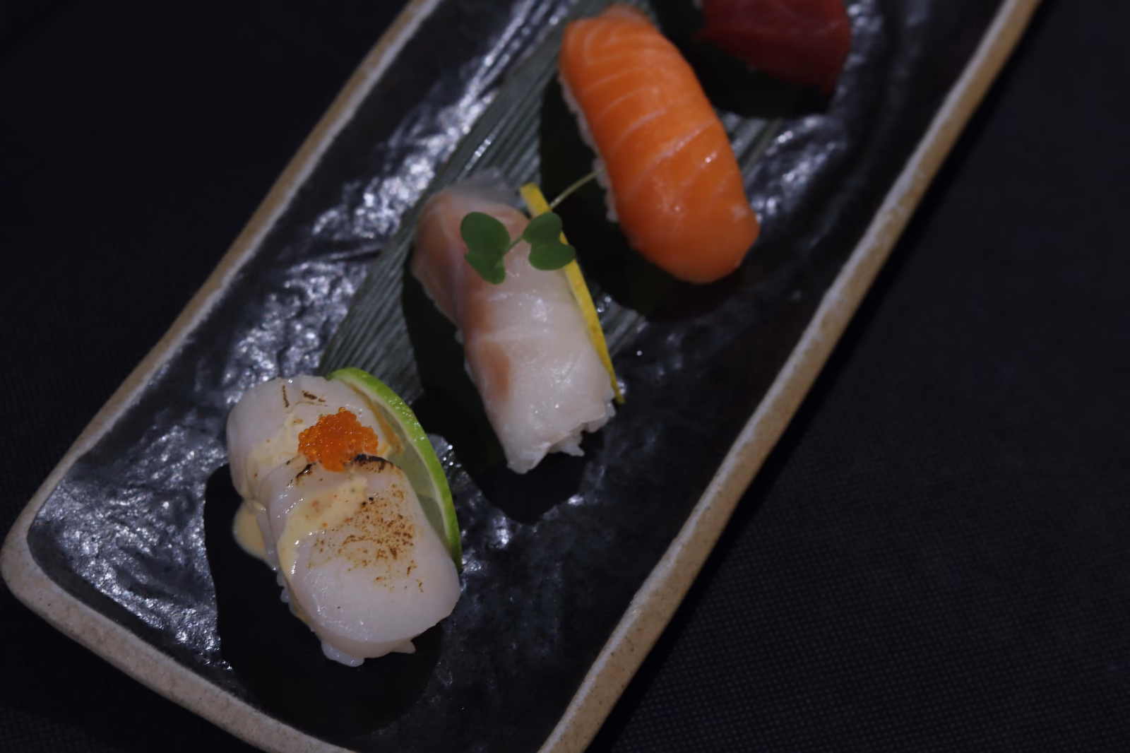 Un surtido de nigiri de vieira, pescado blanco, salmón y atún sobre pizarra en Hito