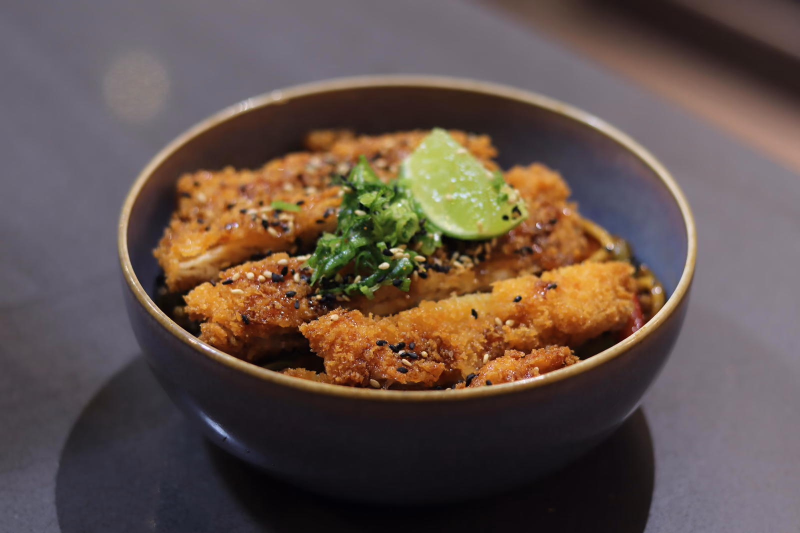 Un bol de pollo katsu crujiente con sésamo, cebolleta y lima en Hito