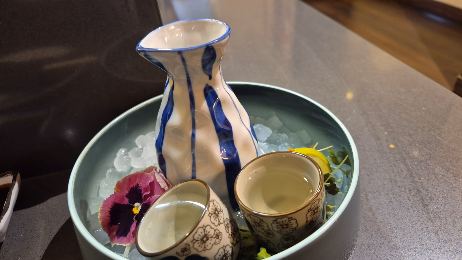 Una jarra de sake y vasos servidos con hielo y flores en Hito