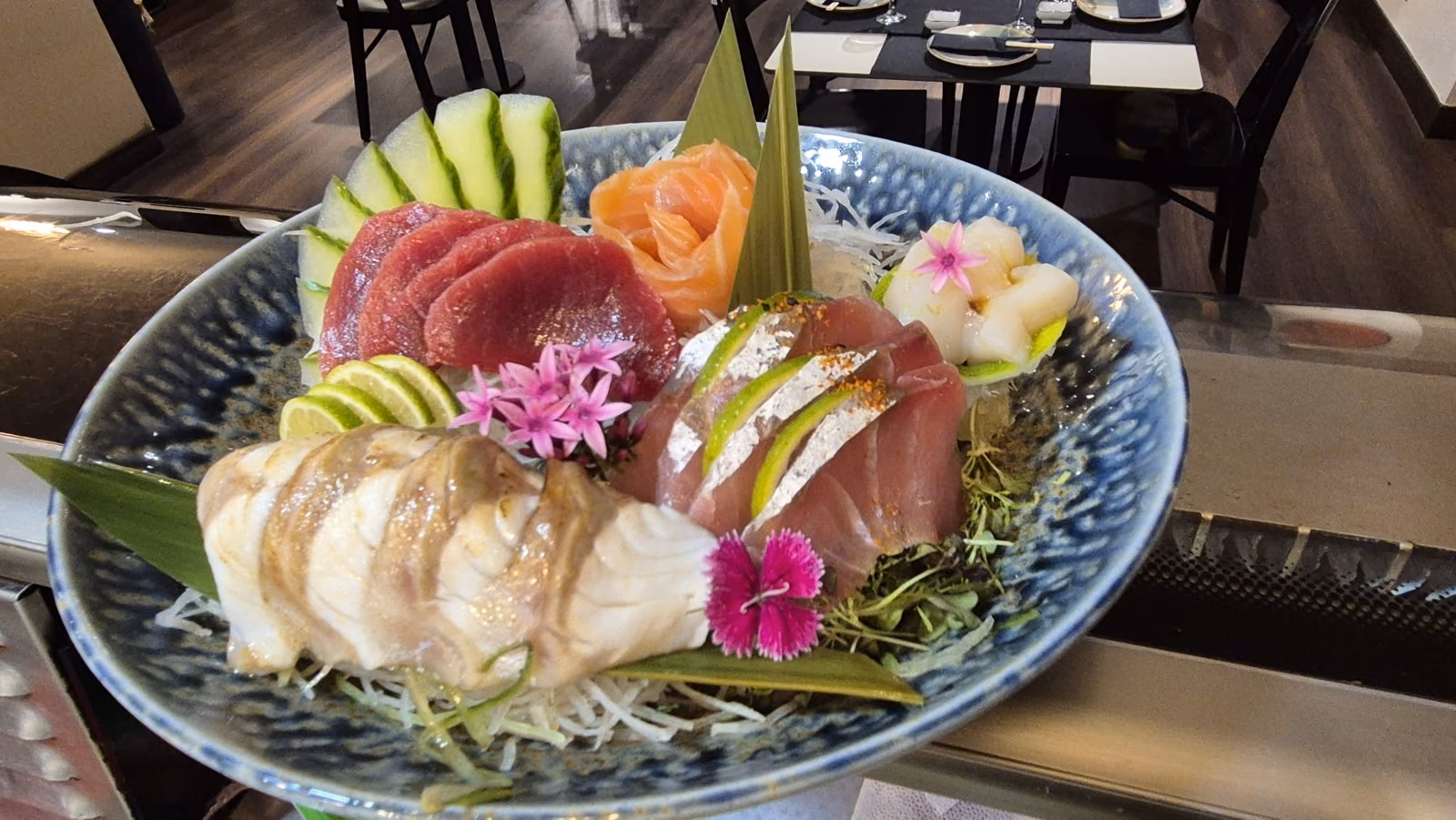 Un bol azul de sashimi variado (atún, salmón y pescado blanco) con flores en Hito