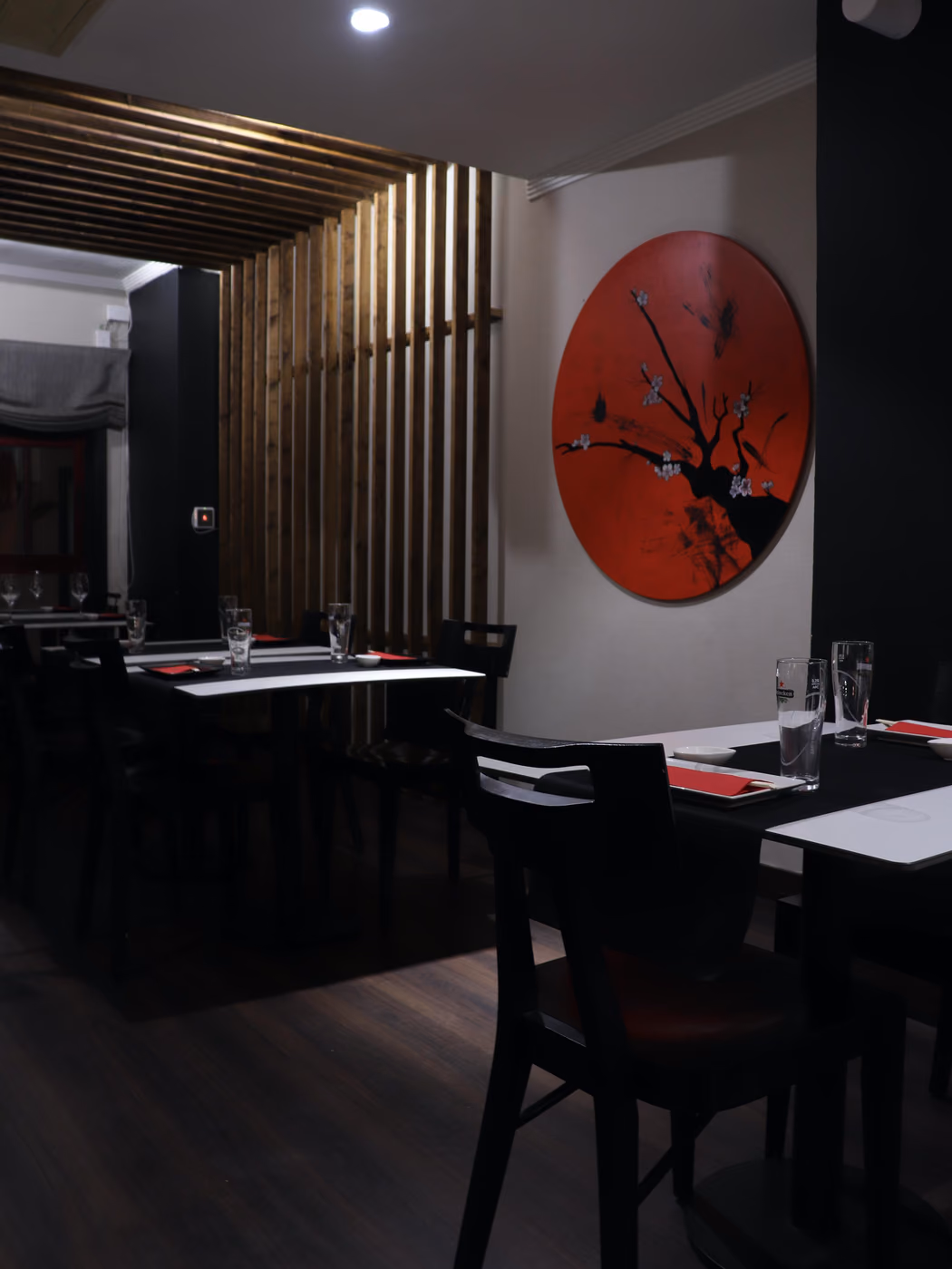 El comedor oscuro e íntimo de Hito en Las Palmas, con una pintura roja de flor de cerezo y un panel de listones de madera