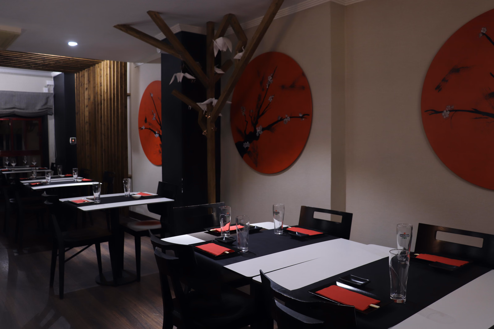 El comedor de Hito en Las Palmas con arte de discos rojos de flor de cerezo, una columna de madera con una grulla y mesas vestidas con servilletas rojas